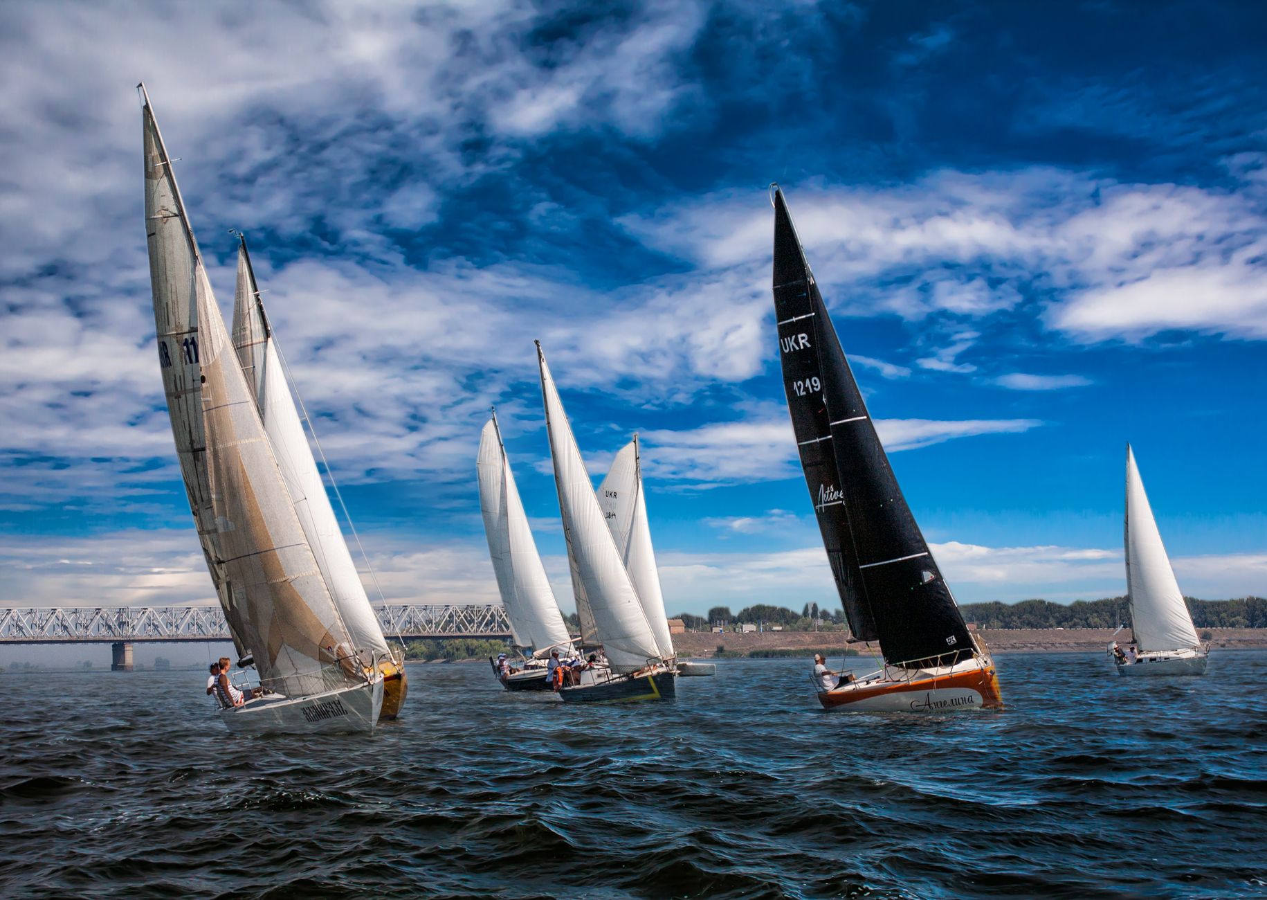 Dynamic image of sailboats racing under blue skies on a scenic lake, showcasing sailing as a thrilling water sport.
